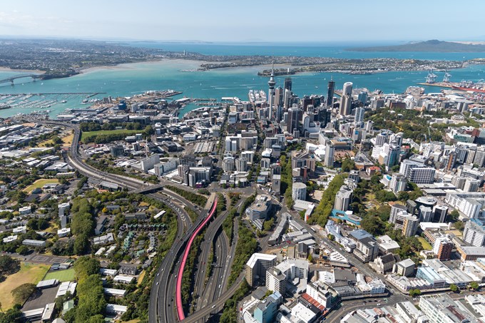 Auckland From Above With The Bright Pink Te Ara I Whiti The Lightpath Visible Leading Into The City With Skytower Prominent