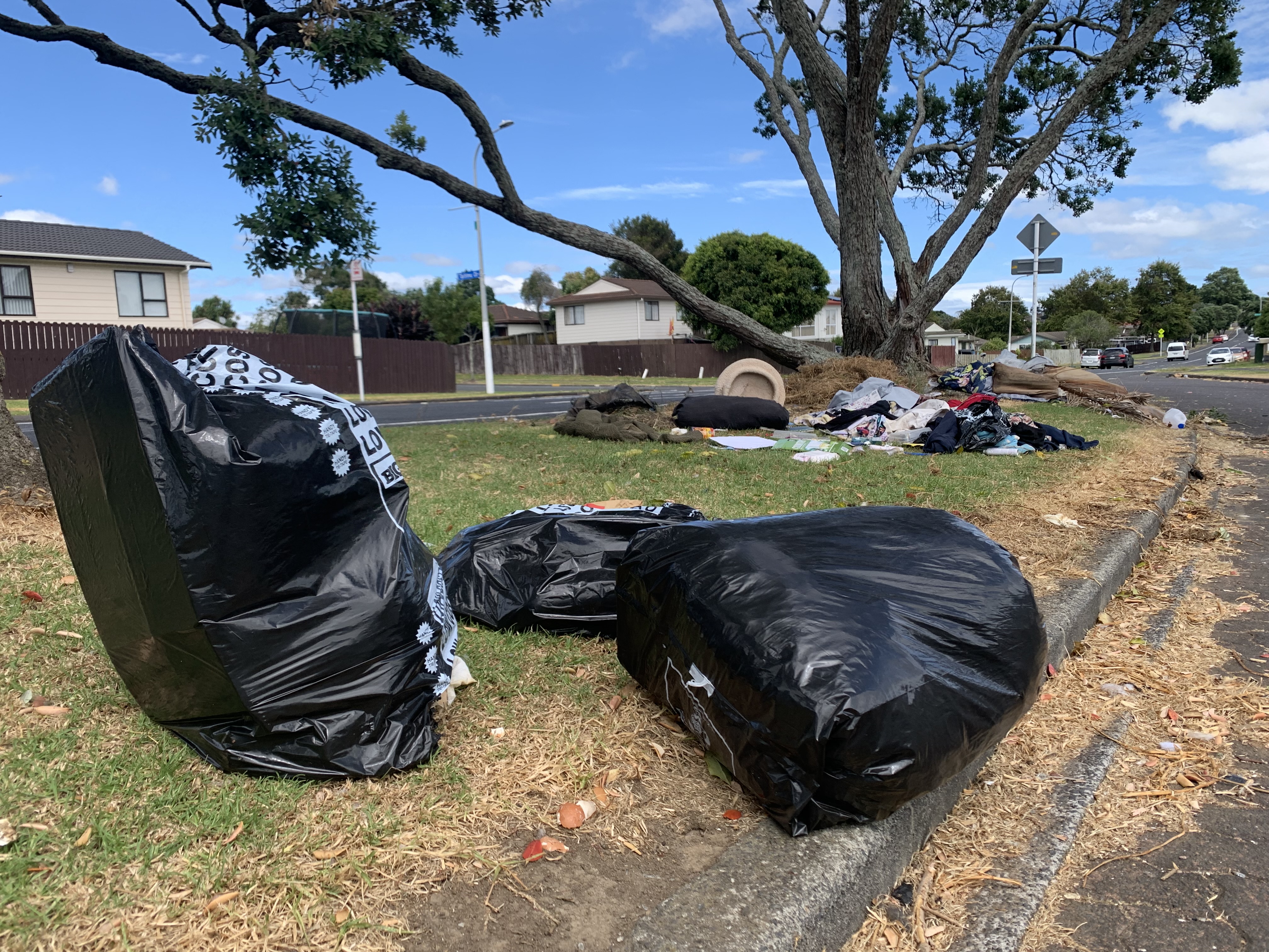 Rubbish bags, clothes and waste strewn over a traffic island on a residential street.