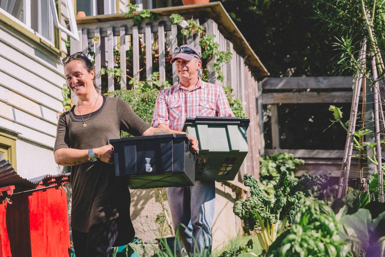 Two people carrying plastic crates in a garden. 
