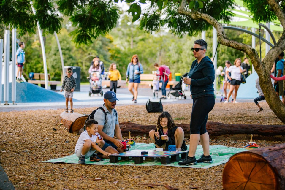 A family having a picnic on a green rug by the playground at Western Springs Park, Auckland.