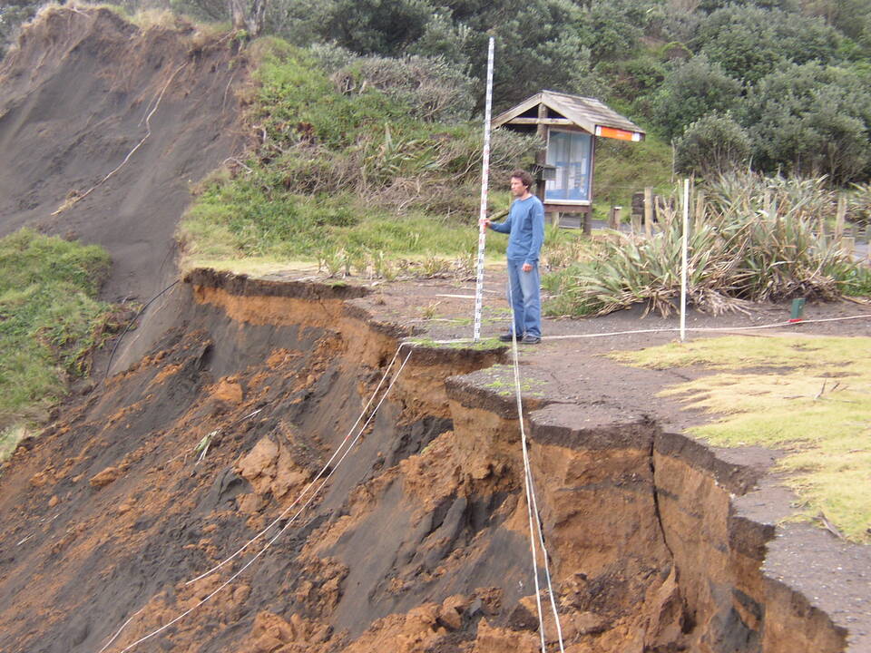 A man overlooking a landslide affected road that has been destroyed. 
