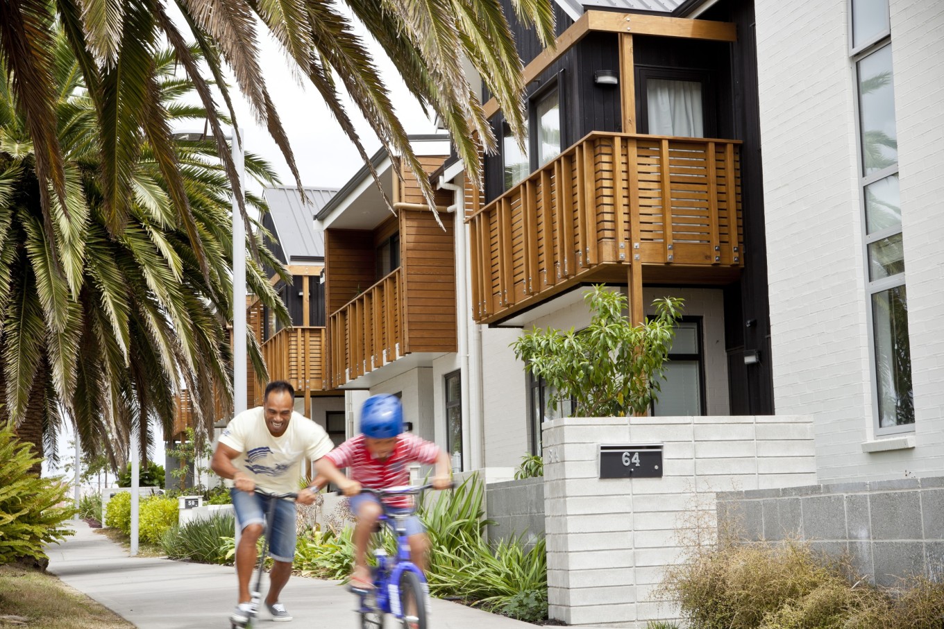 A dad and his child riding their scooter and bike through the local neighbourhood. 