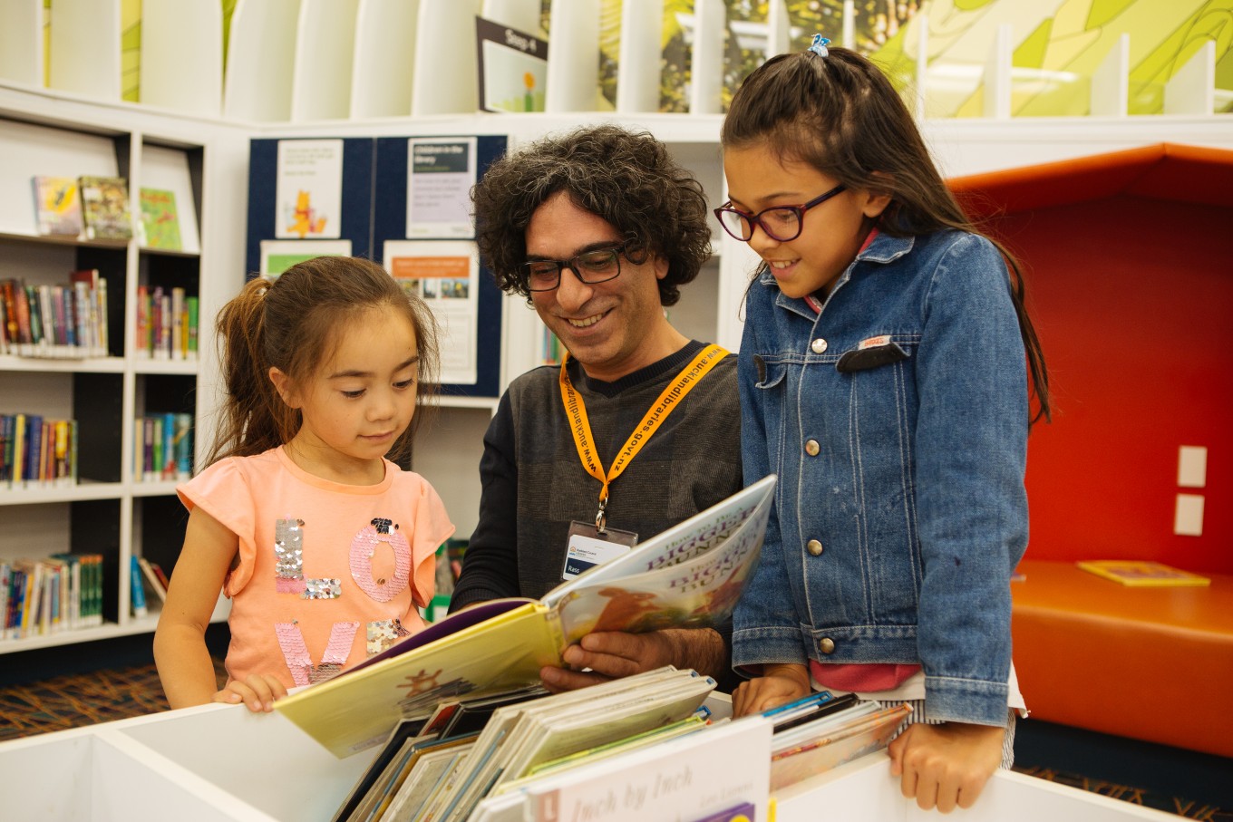 A man reading a book to two little girls at the library.