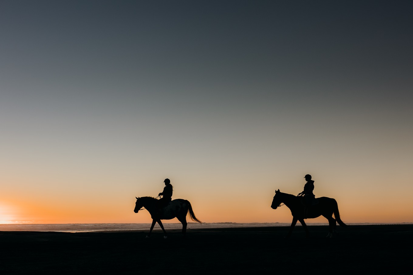 Two horse riders on the beach at sunset. 