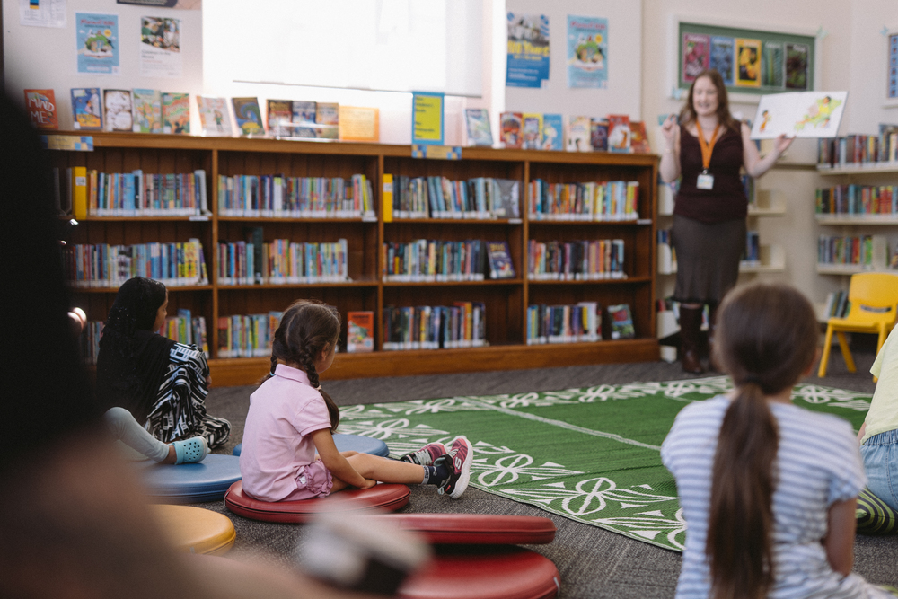 Children sitting on cushions on the floor while someone reads to them.