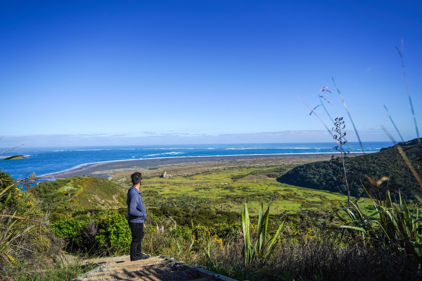 Man looks over Omanawanui Beach from ridge