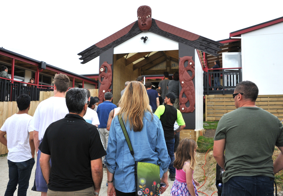 A group of people assemble at the waharoa of Te Herenga Waka O Orewa Marae