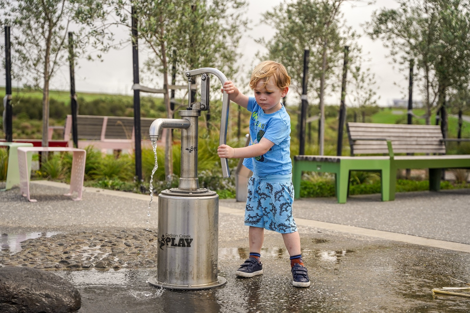 A child playing water pumps (one of which is wheelchair accessible) in the water play area of the Kopupaka playground.