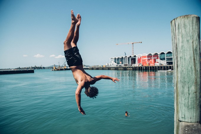 A man mid air jumping off the wharf into the water on a sunny day in Auckland_ivzir0xu.jpg