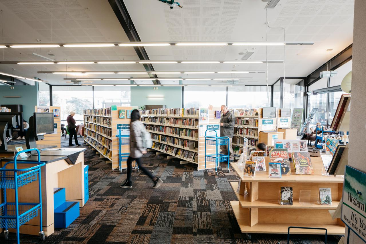 People walking through a shelf section of books at a local library. 