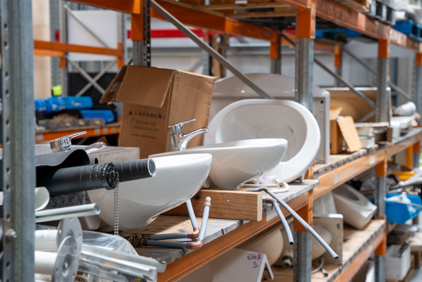 Old toilet seats and sinks on a shelf in a warehouse.