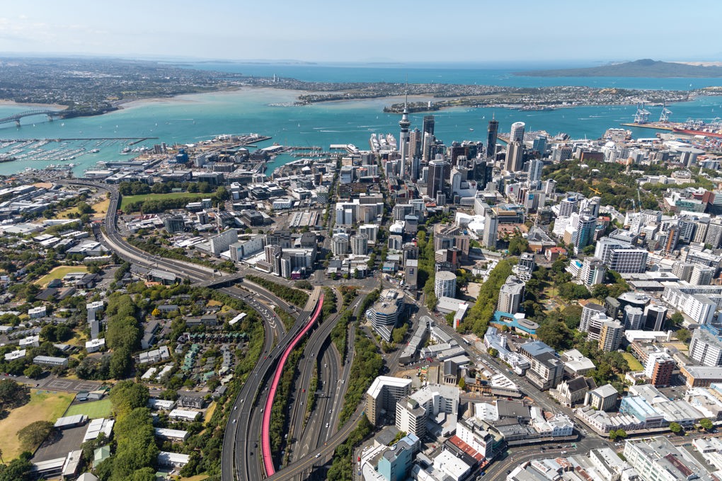 Auckland From Above With The Bright Pink Te Ara I Whiti The Lightpath Visible Leading Into The City With Skytower Prominent