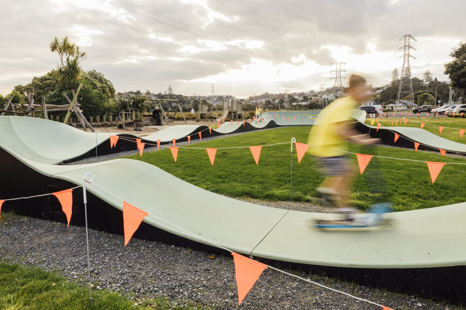 Young person scootering past on Onehunga Bay Reserve pump track