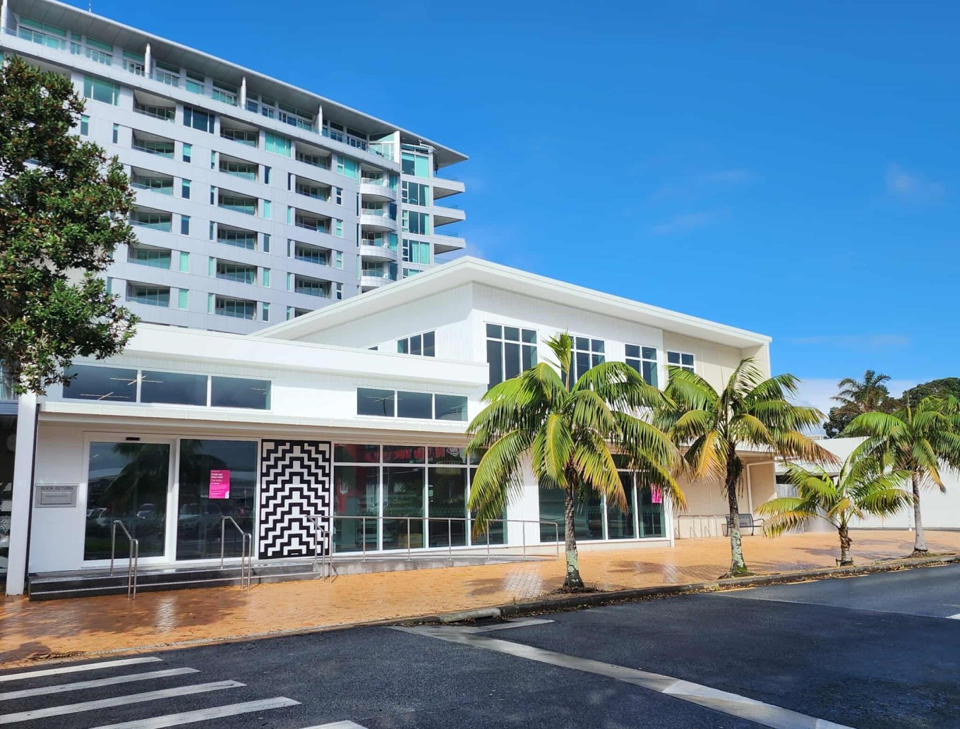 The outside of the community hub on a sunny day with palm trees out the front by a carpark.