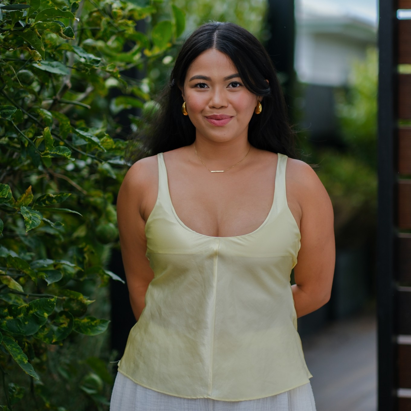 A lady standing in front of a hedge. 