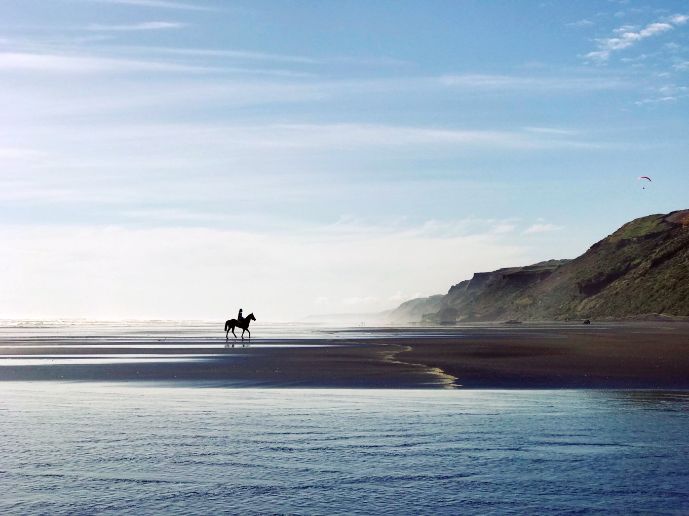 A person riding a horse at Karioitahi Beach by the water. 